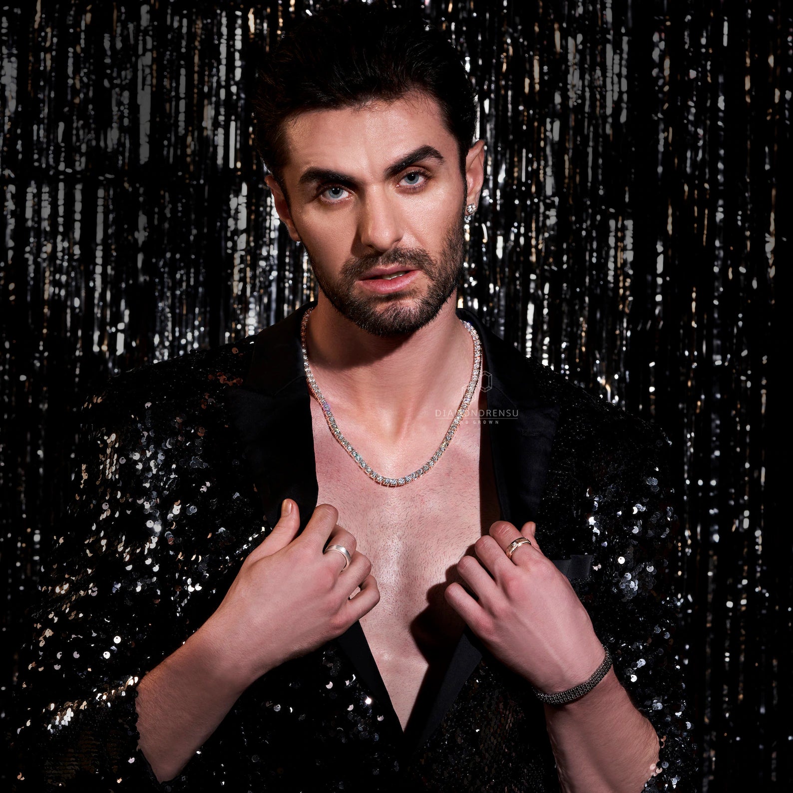 Man wearing a black sequin outfit with a shiny background